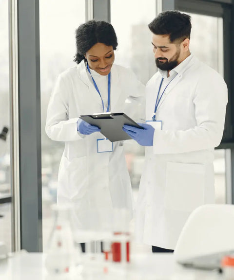 Two lab professionals in white coats and gloves discussing data on a clipboard, symbolizing tailored solutions and collaboration in a laboratory setting.