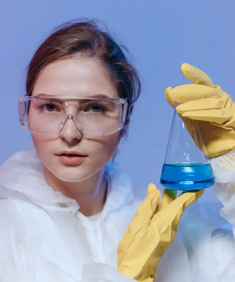 A scientist wearing safety goggles, a protective suit, and yellow gloves holding a conical flask with blue liquid for the food industry